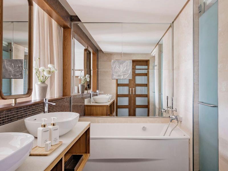 Moderne badkamer met bad, wastafel en grote spiegel in warme houttinten.