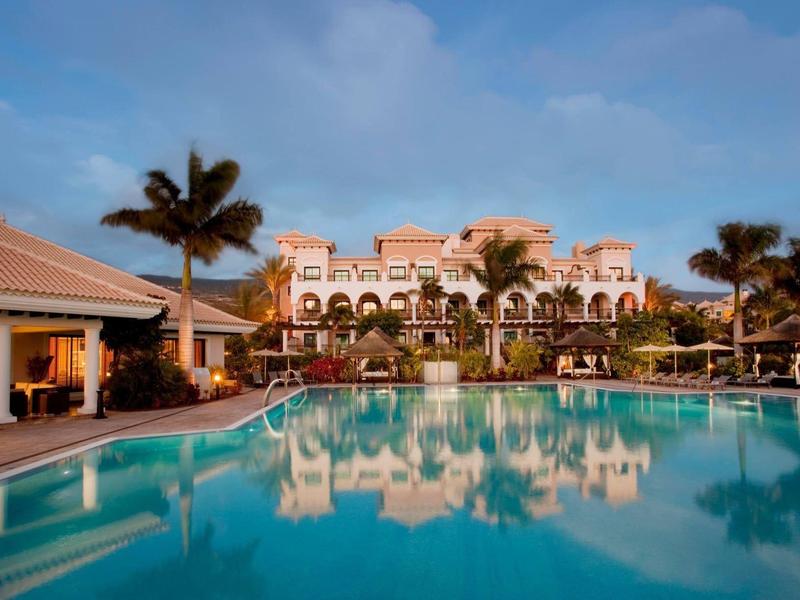 Luxe hotel met palmbomen en groot zwembad bij zonsondergang.