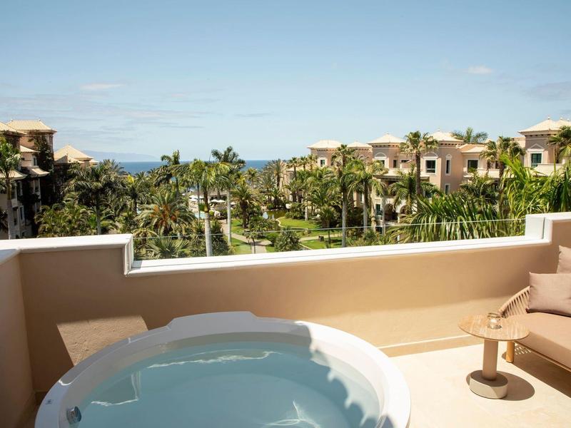 Uitzicht vanaf terras met bubbelbad op groene hotelomgeving en blauwe lucht.