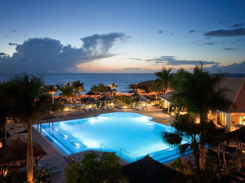 Modern hotelkamer met groot bed, gouden hoofdeinde en neutrale kleuren.