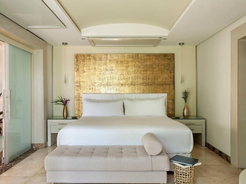 Modern hotelkamer met groot bed, gouden hoofdeinde en neutrale kleuren.