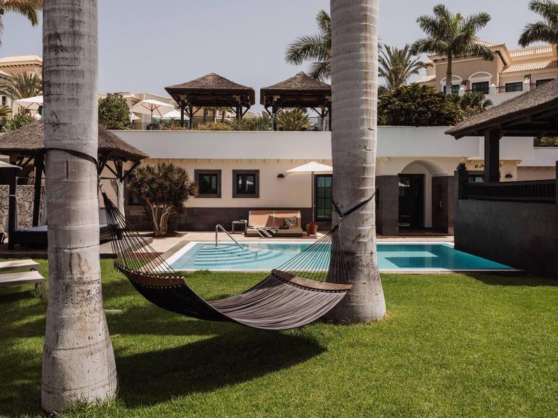 Ontspannende hangmat tussen palmbomen naast een zwembad in een hotel tuin.