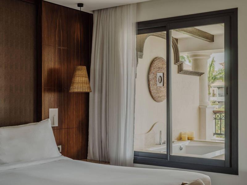 Moderne hotelkamer met tweepersoonsbed, houten accenten en uitzicht op terras door groot raam.