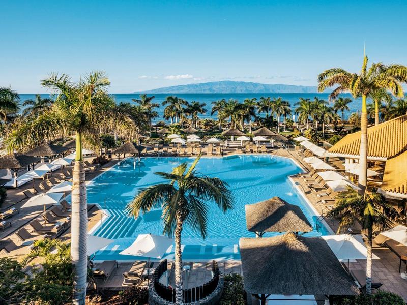 Zwembadgedeelte van een resort met palmbomen, ligstoelen en zeezicht.