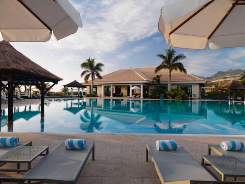 Luxe zwembadgebied met ligstoelen, parasols en tropisch uitzicht bij een resort.