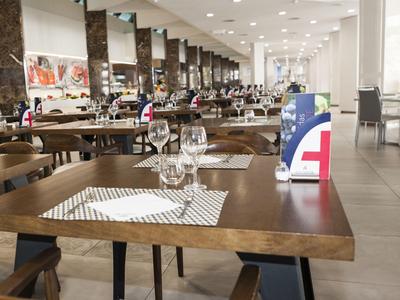 Großes modernes Restaurant mit Holztischen, Stühlen und dekorierten Tischen in hellem Raum.