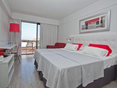 Modernes Hotelzimmer mit Doppelbett, rotem Akzent, Schreibtisch, Balkon und Meerblick.