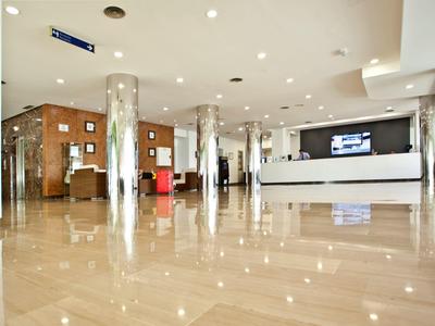 Großer heller Empfangsbereich mit glänzendem Marmorboden, Säulen und moderner Rezeption in Weiß.