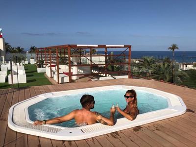 Due persone si rilassano in una vasca idromassaggio con vista sul mare e sull'area dell'hotel.