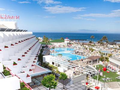 Vista di un hotel a terrazze, piscina e mare sotto un cielo azzurro.