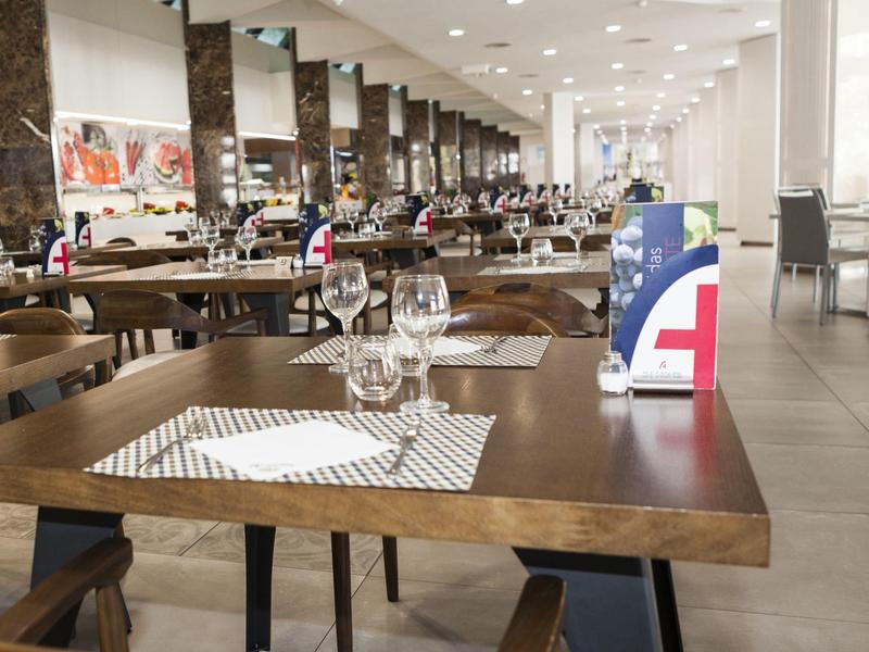 Großes modernes Restaurant mit Holztischen, Stühlen und dekorierten Tischen in hellem Raum.