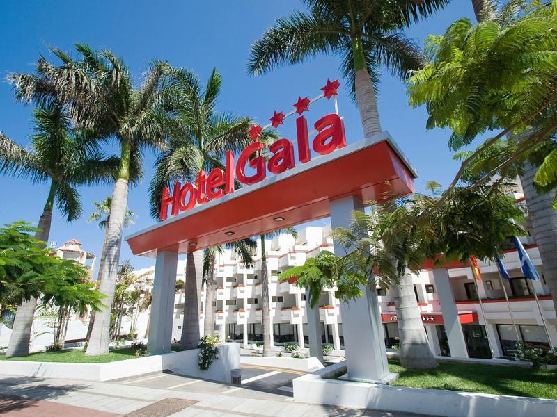 Eingang vom Hotel Gaia mit roten Buchstaben, weißen Säulen und Palmen bei klarem Himmel.