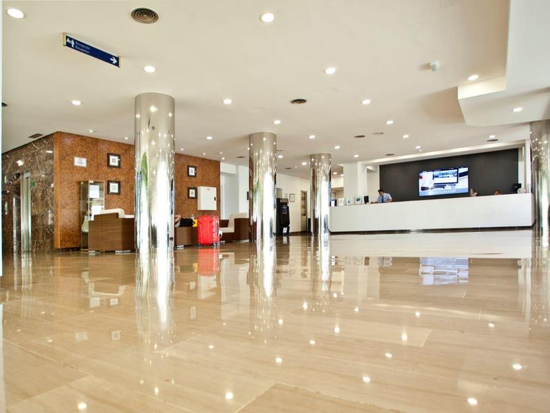 Großer heller Empfangsbereich mit glänzendem Marmorboden, Säulen und moderner Rezeption in Weiß.