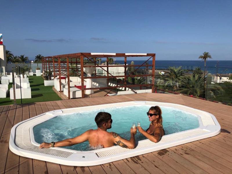 Zwei Personen entspannen sich im kleinen weißen Whirlpool auf Holzterrasse mit Meerblick.