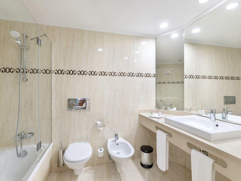 Helles Badezimmer mit Badewanne, Toilette, Bidet, großem Spiegel und Doppelwaschbecken.