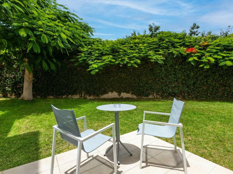 Zwei graue Stühle und ein runder Tisch stehen auf einer Terrasse, umgeben von grünen Bäumen und Rasen.