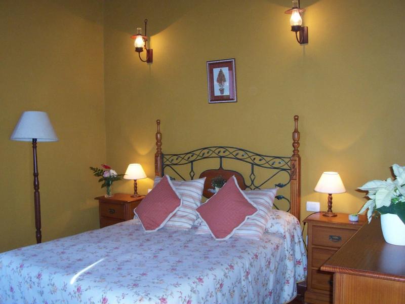 Ein gemütliches Schlafzimmer mit gelben Wänden, Doppelbett, Nachttischen, Lampen und Dekokissen.