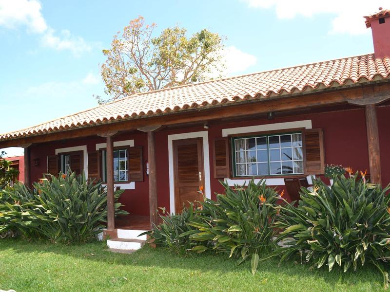 Ein einstöckiges rotes Haus mit weißen Fenstern, umgeben von grünen Pflanzen und Rasen.