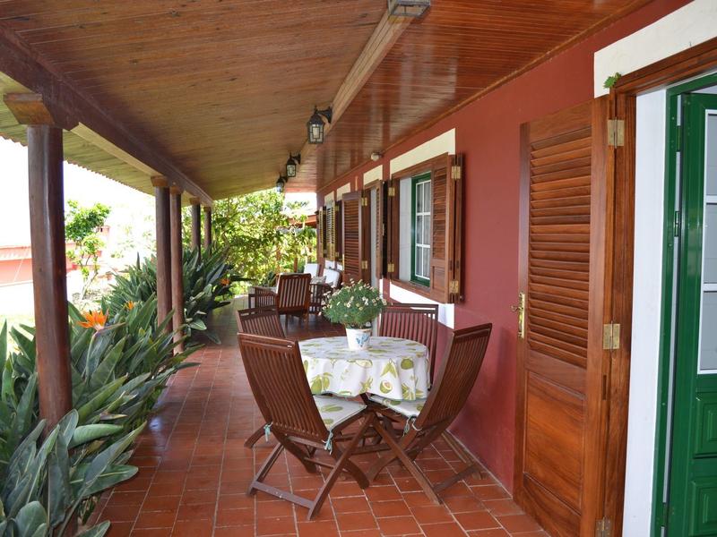 Überdachte Terrasse mit Holzmöbeln, roten Fliesenboden und Pflanzen entlang der Seite.