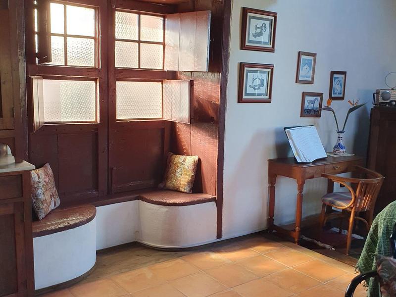 Příjemný kout s dřevěnými lavicemi, polštáři a malým dřevěným nábytkem v místnosti s dlaždicovou podlahou.