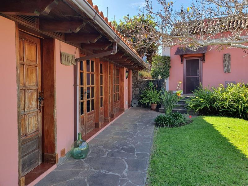 Dvůr s červenými zdmi, dřevěnými dveřmi a okny, kamennou terasou a trávníkem.