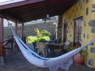 Zadaszony taras z hamakiem, stołem i krzesłami przed domem z żółto-czarną kamienną ścianą.