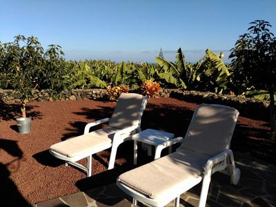 Twee ligstoelen en een tafel op een terras met bananenplanten op de achtergrond.