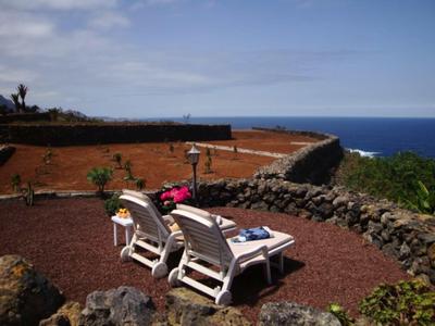 Deux chaises longues sur sol rouge avec vue sur l'océan, entourées de murs en pierre.