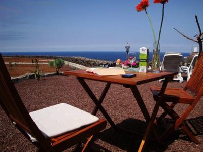 Table et chaises sur terrasse avec vue sur la mer et ciel clair.