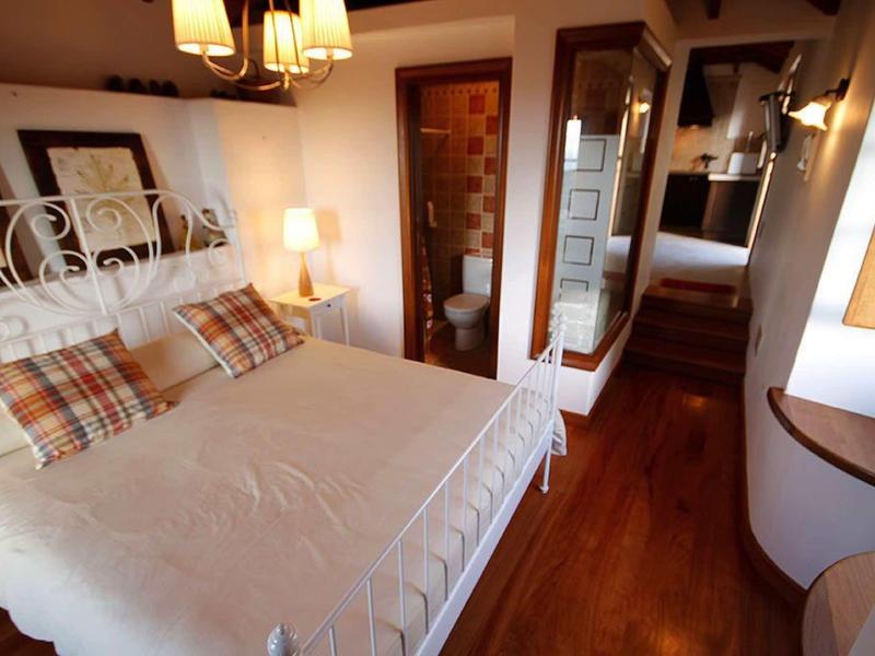 Chambre d'hôtel confortable avec lit double, sol en bois et salle de bain ouverte.