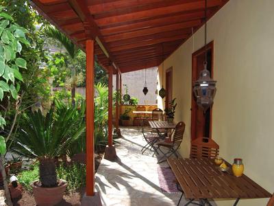 Überdachte Veranda mit Holztischen und Stühlen, Pflanzen und rotbrauner Holzkonstruktion.