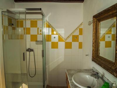 Piccola doccia da bagno con parete in vetro, pareti piastrellate bianco-gialle e specchio sopra il lavabo.