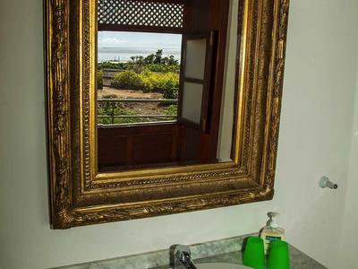 Un lavandino bianco con rubinetto su un piano in marmo sotto uno specchio con cornice dorata su una parete bianca.