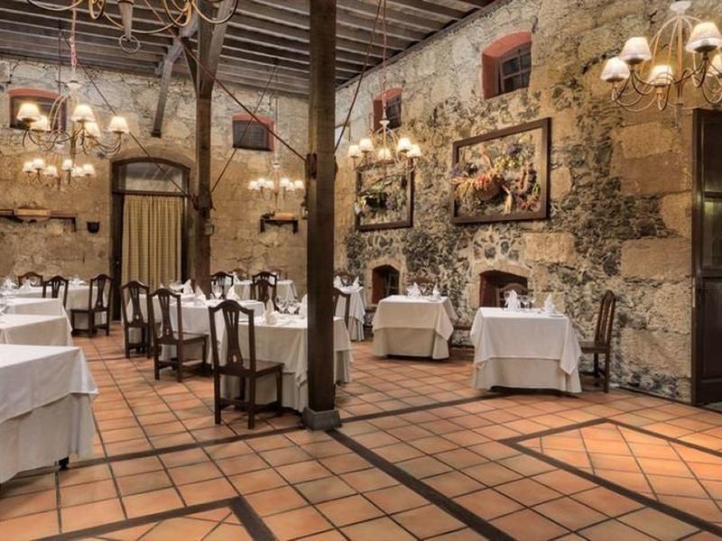 Ristorante rustico con pareti in pietra, soffitto con travi in legno e tavoli apparecchiati con tovaglie bianche.