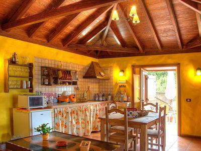 Gemütliche Landhausküche mit Holzdecke, gelben Wänden, Esstisch und offenem Fenster zum Garten.