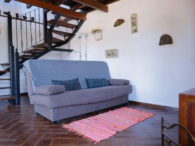 Gemütliches Wohnzimmer mit grauem Sofa, buntem Teppich und offener Treppe aus Holz und Metall.