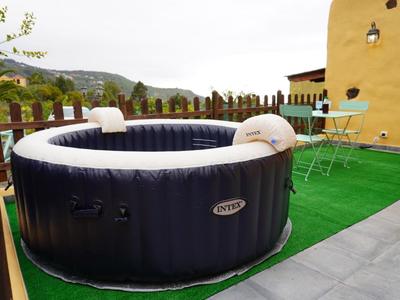 Aufblasbarer Whirlpool auf grünem Kunstrasen neben hausgelber Wand auf Terrasse mit Metalltisch und Stühlen.