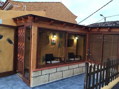 Ein Hauseingang mit verglaster Terrasse, Holztür und Lattenzaun, warm beleuchtet.