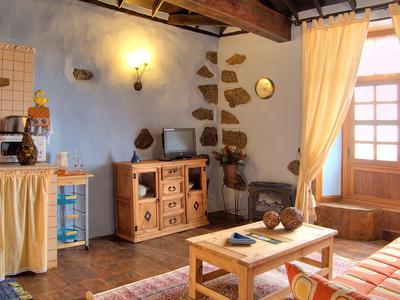 Gemütliches Wohnzimmer mit Holzbalken, Holzmöbeln, blauen Wänden und großen Fenstern mit Vorhängen.