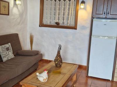 Gemütliches Wohnzimmer mit braunem Sofa, Holztisch, Kühlschrank und Fliesenboden unter Dachschräge.