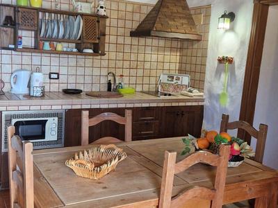 Rustikale Küche mit Holzdecke, Holztisch, vier Stühlen und Küchenregalen mit Geschirr.