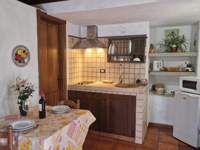 Kleine Küche mit Holzmöbeln, Fliesenrückwand, Esstisch mit Blumen und Flaschen, weiße Wände.