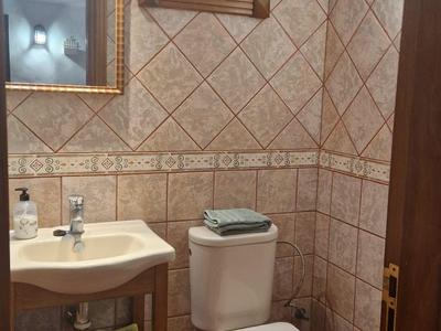 Kleines Bad mit braunen Wandfliesen, weißem WC, Waschbecken und Holzmöbel mit Spiegel.