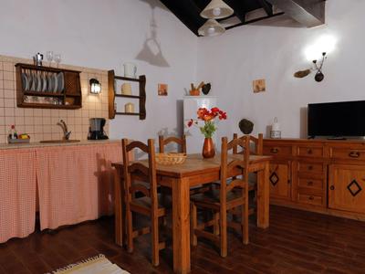 Küche und Esszimmer mit Holzmöbeln, Ziegelboden, Tisch, Stühlen und Küchenschränken mit Vorhängen.