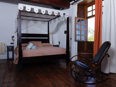 Gemütliches Schlafzimmer mit Himmelbett, Holzboden, Schaukelstuhl und offener Balkontür.