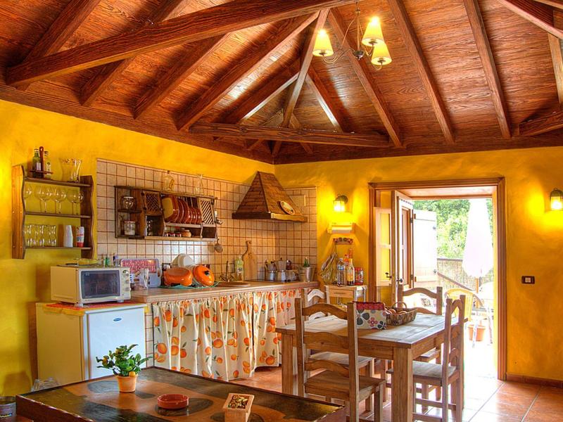 Gemütliche Landhausküche mit Holzdecke, gelben Wänden, Esstisch und offenem Fenster zum Garten.