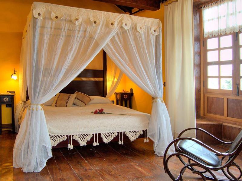 Gemütliches Schlafzimmer mit Baldachinbett, Holzboden, warmen Wänden und einem Schaukelstuhl.