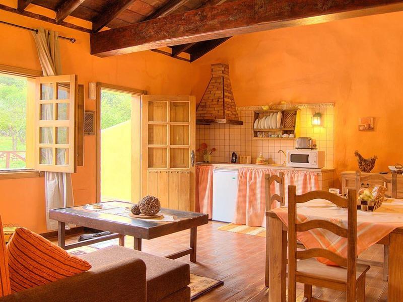 Helles Wohnzimmer mit Holzdecken, offenen Fenstern, Küchenzeile und rustikalen Holzmöbeln.