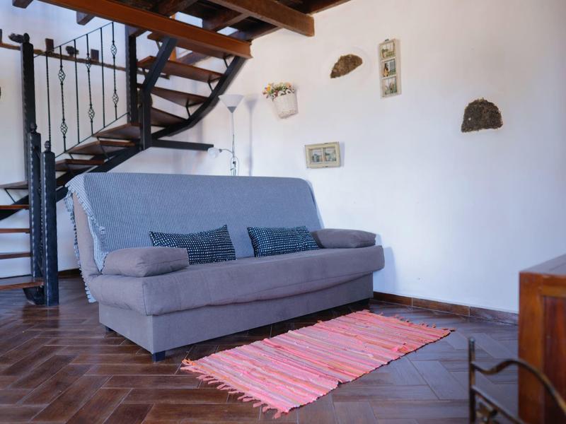 Gemütliches Wohnzimmer mit grauem Sofa, buntem Teppich und offener Treppe aus Holz und Metall.