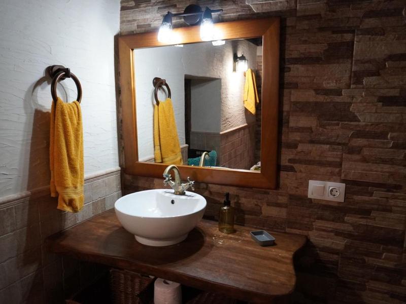 Bad mit rundem weißen Waschbecken, Holztisch, großem Spiegel und gelbem Handtuch an der Wand.